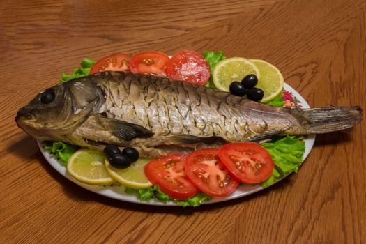 The photo shows a fish on a plate with tomatoes and olives