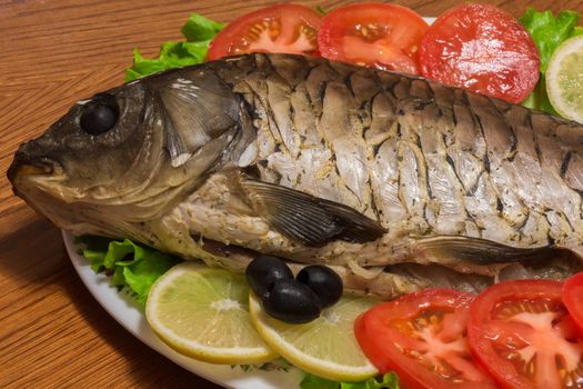 The photo shows a fish on a plate with tomatoes and olives