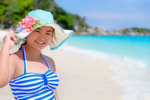 Tourist girl in blue white striped swimsuit standing pose with happy on the beautiful beach and sea during summer at Koh Miang Island, Mu Ko Similan National Park, Phang Nga Province, Thailand