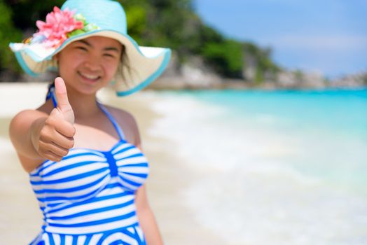 Tourist girl in blue white swimsuit standing thumb up praising the natural beauty of the sea on beach during summer at Koh Miang Island, Mu Ko Similan National Park, Phang Nga Province, Thailand