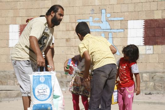 YEMEN, Taiz: A Yemeni man and children carry bags of supplies during a distribution of food and clean water in the Nasser school, outside Taiz (Ta'izz), western Yemen, on October 23, 2015. Many Yemenis are suffering from lack of basic services and resources, in a humanitarian disaster dramatically worsened by a blockade imposed by the Saudi-led coalition.