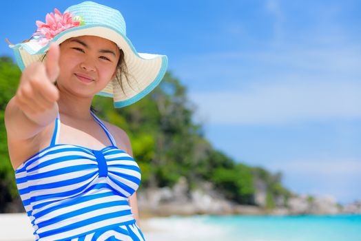 Tourist girl in blue white swimsuit standing thumb up praising the natural beauty of the sea on beach during summer at Koh Miang Island, Mu Ko Similan National Park, Phang Nga Province, Thailand