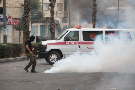WEST BANK, Hebron: A Palestinian protester moves a tear gas canister aside from an ambulance during clashes between Palestinians and Israeli security forces on October 23, 2015, following Friday prayers, in Ras e-Jura, in the northern entrance of Hebron, West Bank. Israel lifted age restrictions for the main weekly prayers at Jerusalem's flashpoint Al-Aqsa mosque compound, in an apparent bid to ease tensions over the site that sparked a surge in Israel-Palestinian violence. 