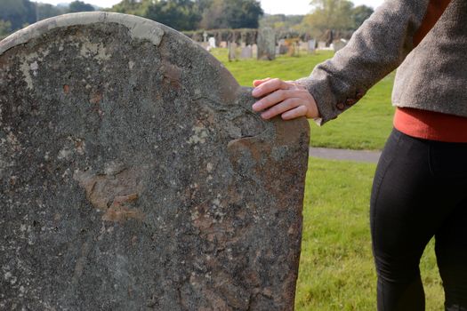 Woman's hand resting on an anonymous headstone in a rural graveyard