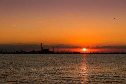 Sea sunset with silhouettes of a chemical industrial hub.