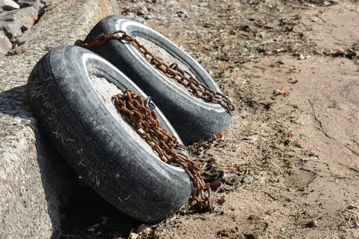 Two old tires chained to a wall on a beach