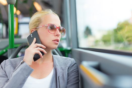 Blonde caucasian business woman talking on cell phone, traveling by bus. Public transport and commuting to work.