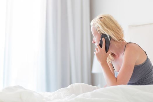 Portrait of  young lady with mobile phone in bed at home. Tired sleepy woman receiving emergency call in bed early in the morning.