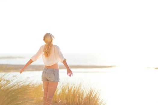 Relaxed woman enjoying freedom and life an a beautiful sandy beach.  Young lady feeling free, relaxed and happy. Concept of happiness, enjoyment and well being.  Enjoying Sun on Vacations. Copyspace.