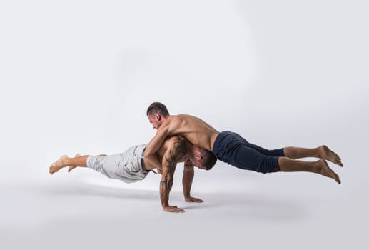 Muscular Shirtless Male Acrobatic Dancers Balancing on Top of Each Other in Studio with White Background