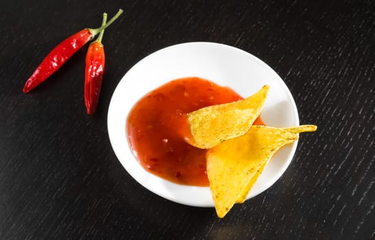 crisp corn nachos with spicy hot tomato sauce as a snack or appetizer in a white disc on black wood table