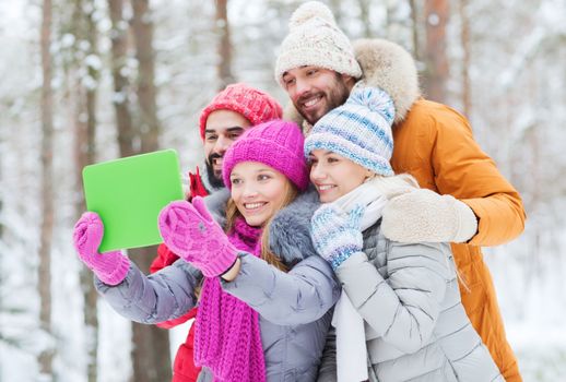 technology, season, friendship and people concept - group of smiling men and women taking selfie tablet pc computer in winter forest