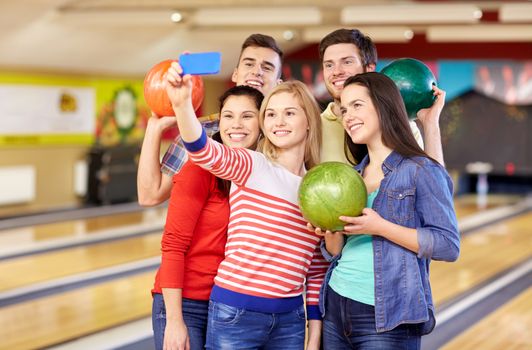 people, leisure, sport, friendship and entertainment concept - happy friends taking selfie with smartphone in bowling club