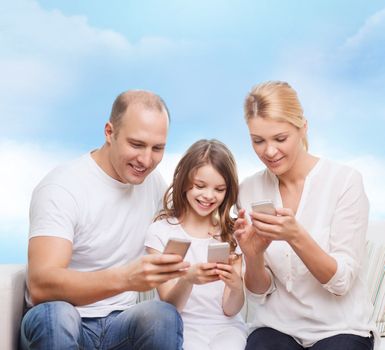 family, technology and people concept - smiling mother, father and little girl with smartphones over blue sky background