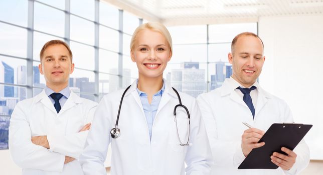 medicine, profession, teamwork and healthcare concept - group of smiling medics or doctors with clipboard and stethoscopes over clinic background