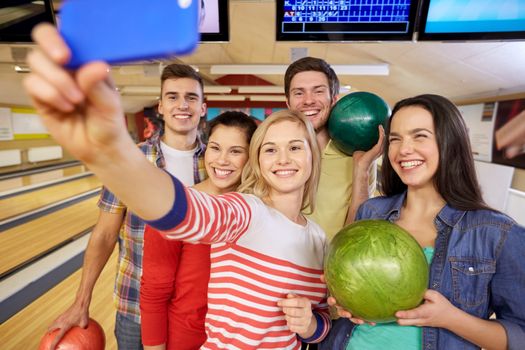 people, leisure, sport, friendship and entertainment concept - happy friends taking selfie with smartphone in bowling club