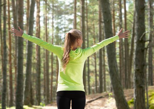 fitness, sport, happiness and people concept - happy woman raising hands over woods background from back