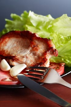 Piece of roasted meat on plate near tomato and green salad