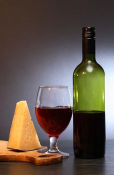 Bottle of red wine near wineglass and piece of cheese on nice gray background