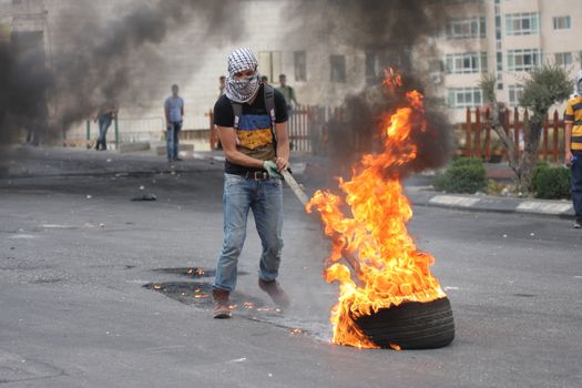 WEST BANK, Ramallah : A Palestinian protester puts the fire to a tyre during clashes with Israeli security forces in the West Bank town of Ramallah, on the road towards Al-Bireh, near Beit El checkpoint, on October 23, 2015. Since October 1, at least 49 Palestinians and one Israeli Arab have been killed, including alleged attackers. Eight Israelis have been killed in attacks.