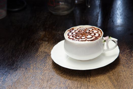 coffee with flower pattern in a white cup on wooden background