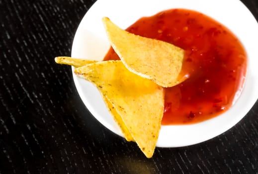 crisp corn nachos with spicy hot tomato sauce as a snack or appetizer in a white disc on black wood table