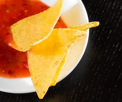 delicious crisp corn nachos with spicy hot tomato sauce as a snack or appetizer in a white disc on black wood table