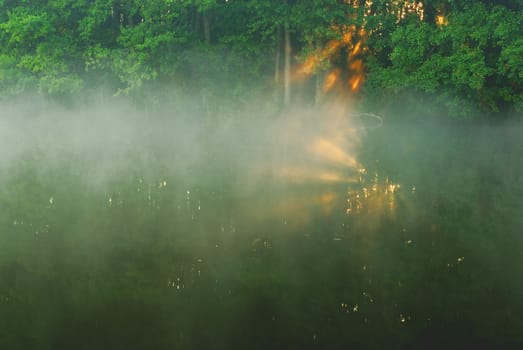 Poland, the morning fog on the river highlighted in red rays of the rising sun.Horizontal view.
