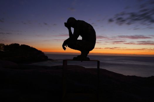 BONDI, AUSTRALIA - OCTOBER 25, 2015;  Annual Sculpture by the Sea free public event.  Exhibit titled Crouching Man by Laurence Edwards.    Made of bronze. Silhouette against dawn sky