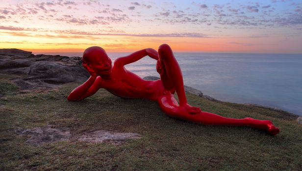 BONDI, AUSTRALIA - OCTOBER 25, 2015;  Annual Sculpture by the Sea  public event.  Exhibit titled Harbour by Chen Wenline, a glossy painted bronze figure with cheeky expression and pose against a sunrise sky