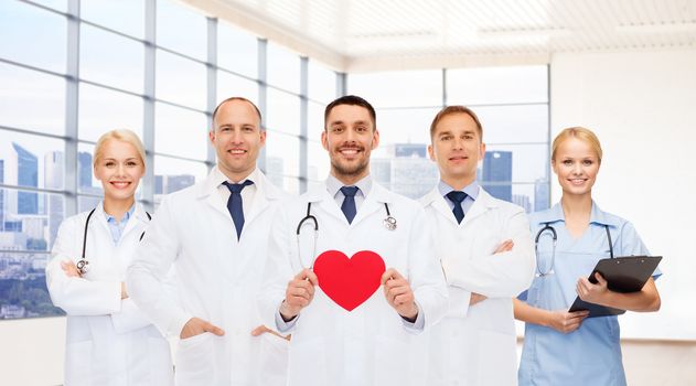 medicine, cardiology, healthcare and people concept - happy young doctors cardiologists with red heart over clinic background