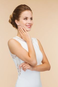 engagenment, celebration, wedding and happiness concept - smiling woman in white dress wearing diamond ring over beige background