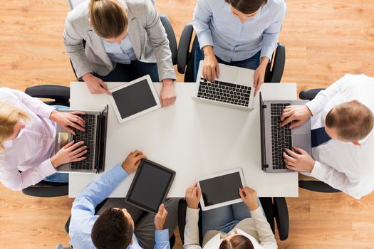 business, people and technology concept - close up of creative team with laptop and tablet pc sitting at table in office