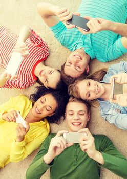 education, technology and happiness concept - group of young smiling people lying down on floor in circle with smartphones