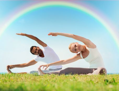 fitness, sport, yoga and people concept - happy couple stretching on mats over rainbow in blue sky background