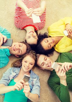 education, technology and happiness concept - group of young smiling people lying down on floor in circle with smartphones