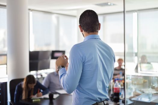 Business man making a presentation at office. Business executive delivering a presentation to his colleagues during meeting or in-house business training. Rear view. Shalow depth of field.