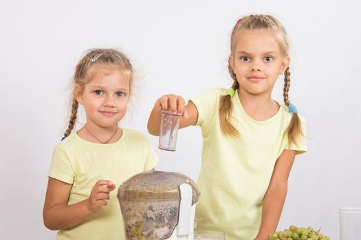 Two girls at a table squeezed juice from pears and grapes with a juicer