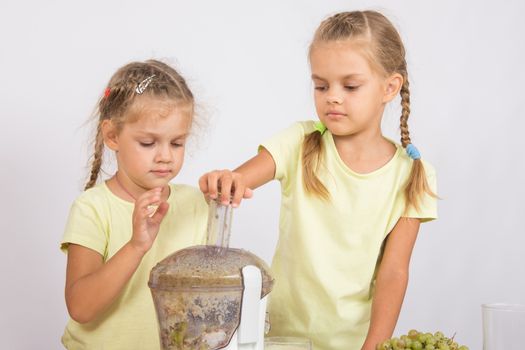 Two girls at a table squeezed juice from pears and grapes with a juicer