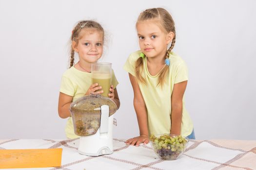Two girls at a table squeezed juice from pears and grapes with a juicer