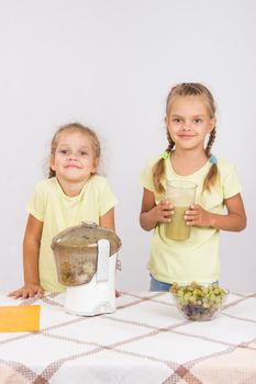 Two girls at a table squeezed juice from pears and grapes with a juicer