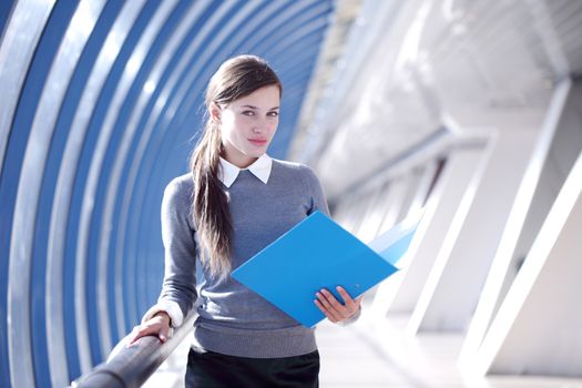 Young Businesswoman with folder standing in corridor of modern office building