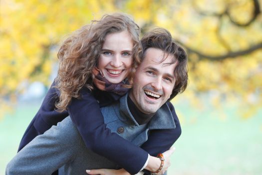 Smiling couple hugging in autumn park on yellow maple tree background