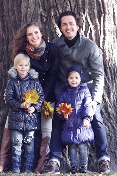 Happy family portrait on big tree background with maple leaves