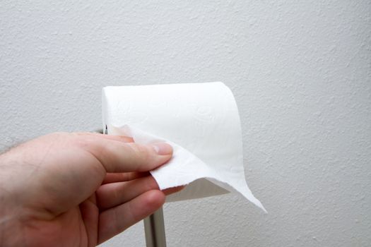 Toilet paper getting ready to be used with a hand grabing it.