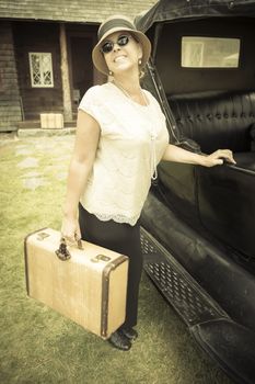 Happy 1920s Dressed Girl Holding Suitcase Next to Vintage Car and Cabin.