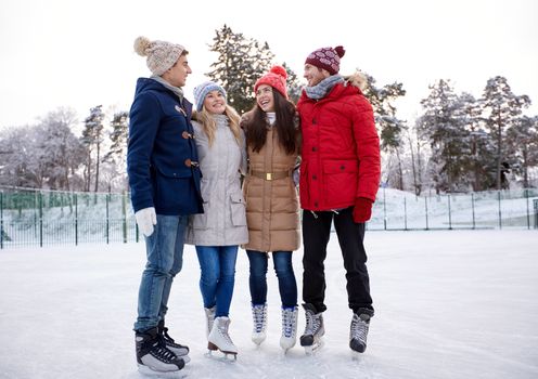 people, winter, friendship, sport and leisure concept - happy friends ice skating and hugging on rink outdoors