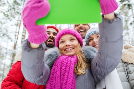 technology, season, friendship and people concept - group of smiling men and women taking selfie tablet pc computer in winter forest