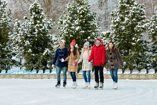 people, winter, friendship, sport and leisure concept - happy friends ice skating on rink outdoors