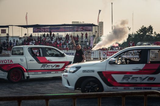 Udon Thani, Thailand - October 18, 2015: Toyota Hilux Revo perform drifting show on the track between the unidentified master of ceremonies in the center at the event Toyota Motor Sport show at Udon Thani, Thailand with smoke and audiences in the background